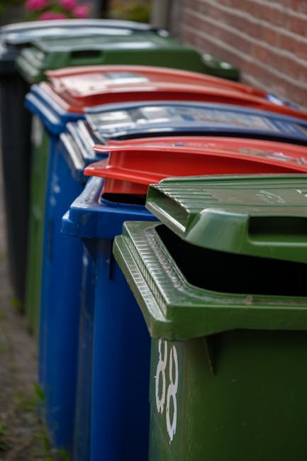 A large collection of mixed household waste and rubbish bags piled outside a designated waste collection area on a paved urban street. The rubbish includes black and transparent plastic bin bags, some