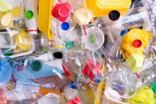A close-up view of a pile of discarded plastic bottles and containers, including transparent, yellow, blue, green, and red caps, with some bottles having labels still attached. The plastic waste is scattered across a flat surface, with bottles overlapping each other, exhibiting various textures from smooth and glossy to crinkled. The background appears to be part of a waste collection or disposal environment, indicating the stage of a rubbish removal process typical for garden clearance services like those provided by Garden Clearance Hendon. The image highlights the variety of plastics often encountered during rubbish clearance tasks, emphasizing the importance of proper disposal and recycling of waste materials in the Hendon area.